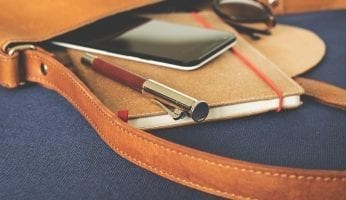 braon torba sa notesom, penkalom, naocarima i mobilnim telefonom